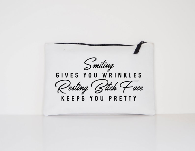 May include: White canvas zippered pouch with black text that reads "Smiling gives you wrinkles, Resting Bitch Face keeps you pretty." The pouch has a black zipper and pull tab.