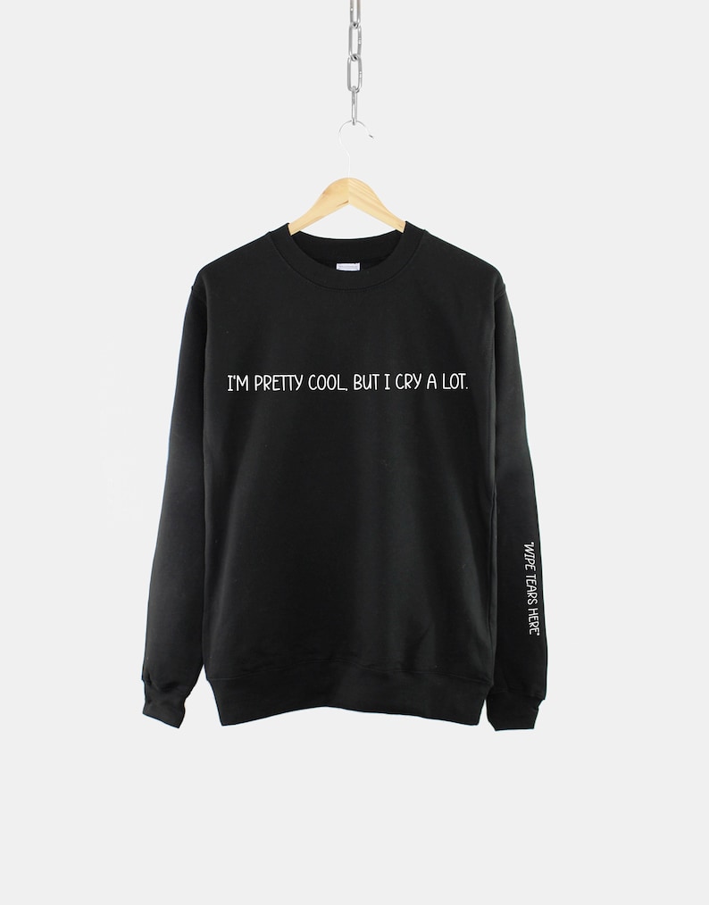 May include: Black sweatshirt with the text "I'm pretty cool, but I cry a lot." printed in white on the front. The text "Wide tears here" is printed in white on the right sleeve.