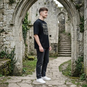 May include: A black short-sleeved t-shirt with white text that reads "WHEN THE DAY SMILES IT'S ALREADY TOO LATE" paired with dark gray jeans and white sneakers. The t-shirt features a crew neckline and a relaxed fit, worn with slim-fit denim pants.