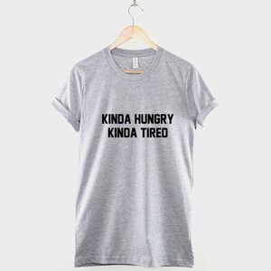 K&ouml;nnte beinhalten: Ein graues T-Shirt mit dem Aufdruck "Kinda Hungry Kinda Tired" in Schwarz.