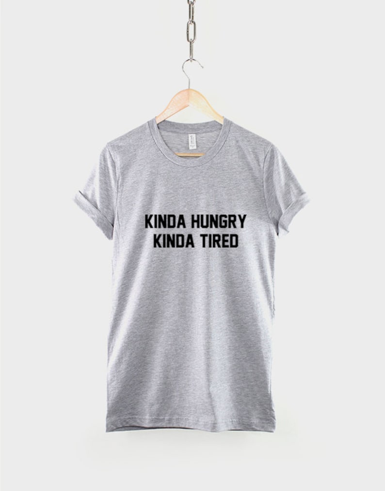 K&ouml;nnte beinhalten: Ein graues T-Shirt mit dem Aufdruck "Kinda Hungry Kinda Tired" in Schwarz.
