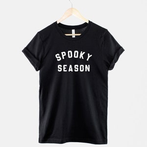Puede incluir: Camiseta negra con texto blanco que dice "Spooky Season" en una fuente universitaria vintage.