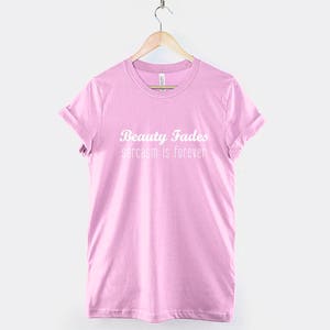 May include: Pink t-shirt with the text "Beauty Fades sarcasm is forever" in white.