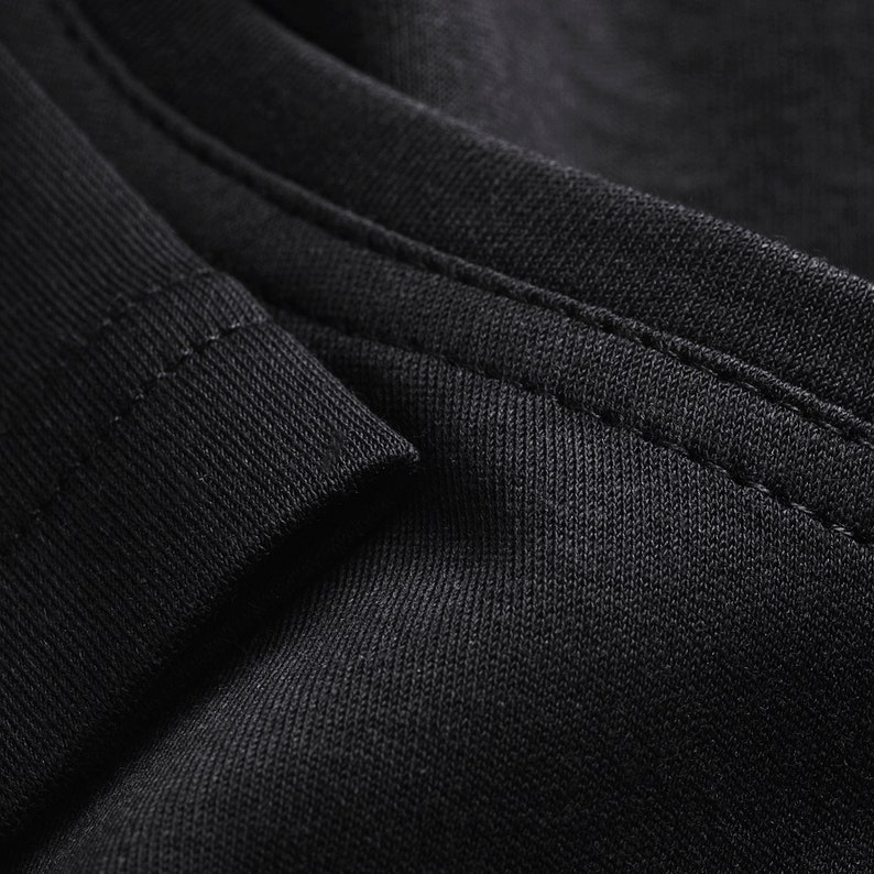 May include: Close-up of black fabric with a stitched seam. The fabric has a textured, woven appearance.
