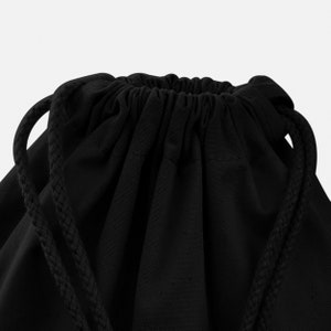 May include: Black drawstring bag made of canvas with a gathered top and long drawstrings.