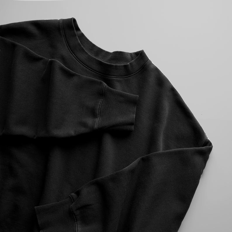 May include: A solid black crewneck sweatshirt featuring a ribbed collar and ribbed cuffs on the long sleeves. The garment is constructed from a smooth, opaque fabric with a consistent matte finish throughout the entire piece of clothing.