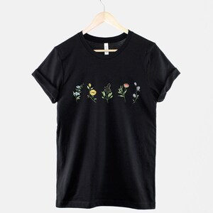 May include: Black t-shirt with a row of five small, colourful floral designs printed across the chest.