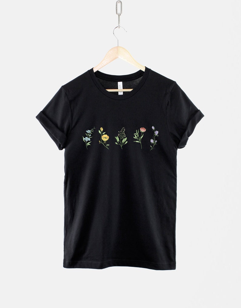 May include: Black t-shirt with a row of five small, colourful floral designs printed across the chest.