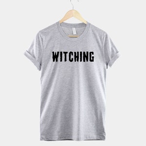 May include: A heather grey t-shirt with the word "Witching" printed in black on the front.