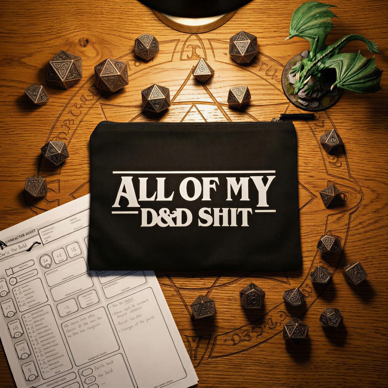 May include: A black rectangular zipped pouch featuring the white text ALL OF MY D&D SHIT printed on the front. The pouch is surrounded by numerous metallic polyhedral dice, a white character sheet, and a small green dragon figurine.