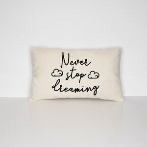 May include: A white throw pillow with black text that reads "Never stop dreaming" with two small cloud drawings on either side of the word "stop".