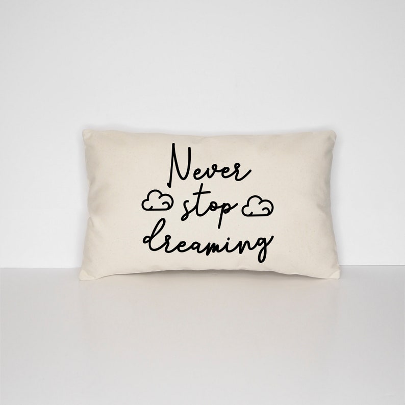 May include: A white throw pillow with black text that reads "Never stop dreaming" with two small cloud drawings on either side of the word "stop".