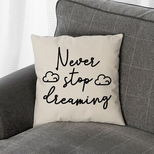 May include: A white throw pillow with black text that reads "Never stop dreaming" with two small cloud drawings on either side of the word "stop".