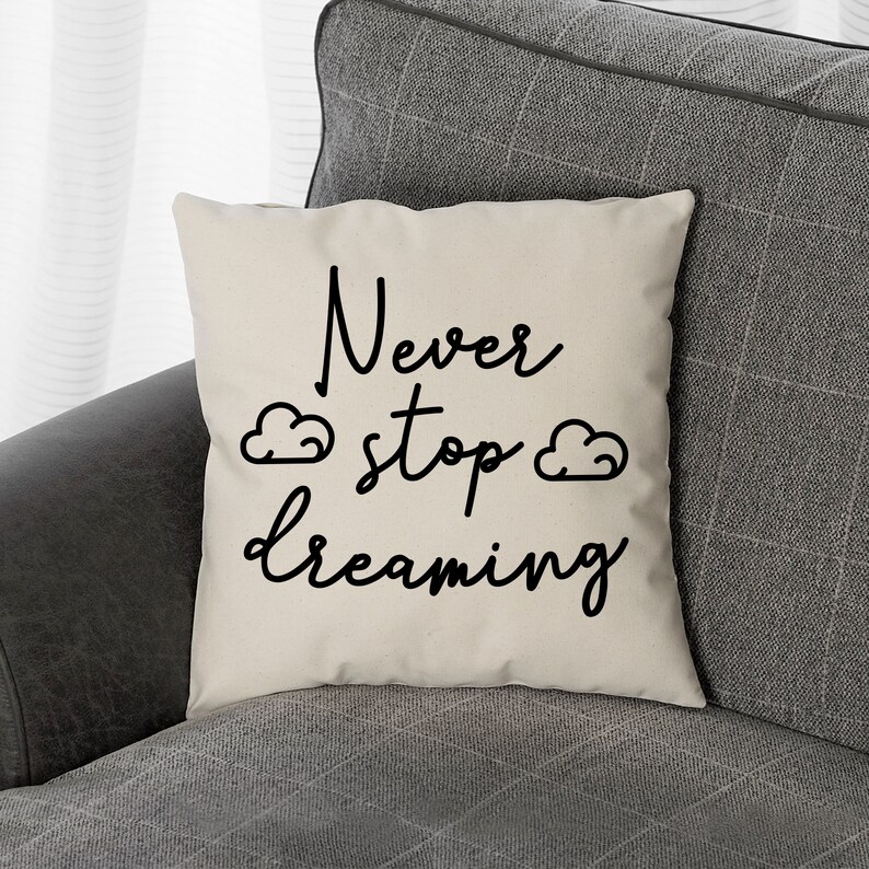 May include: A white throw pillow with black text that reads "Never stop dreaming" with two small cloud drawings on either side of the word "stop".