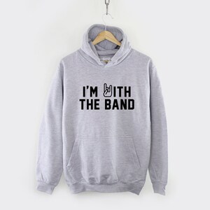Puede incluir: Una sudadera con capucha gris con un gr&aacute;fico negro que dice "I'm with the band" y un gesto de mano de rock and roll.