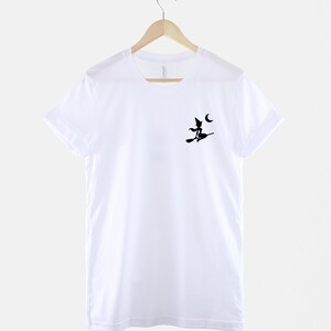 Op de afbeelding: Wit T-shirt met een zwart silhouet van een heks die op een bezem vliegt met een halve maan op de achtergrond.