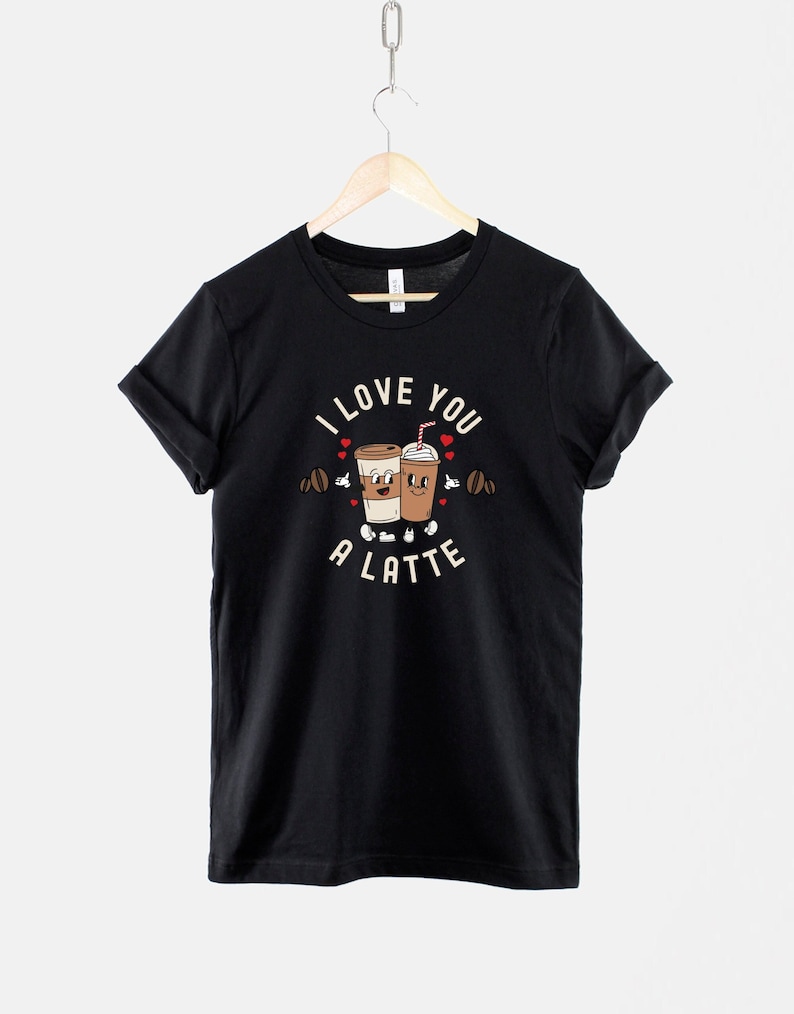 K&ouml;nnte beinhalten: Schwarzes T-Shirt mit einem Motiv von zwei Kaffeetassen, die sich die H&auml;nde halten, und dem Text "I love you a latte".