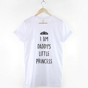 May include: White t-shirt with black text that reads "I am Daddy's Little Princess" and a small crown graphic above the text.
