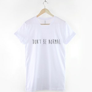 May include: White t-shirt with black text that reads "DON'T BE NORMAL"