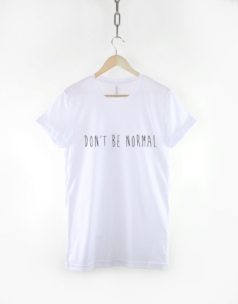 May include: White t-shirt with black text that reads "DON'T BE NORMAL"