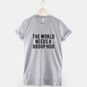 May include: A heather grey t-shirt with the text "THE WORLD NEEDS A GROUP HUG" printed in black.