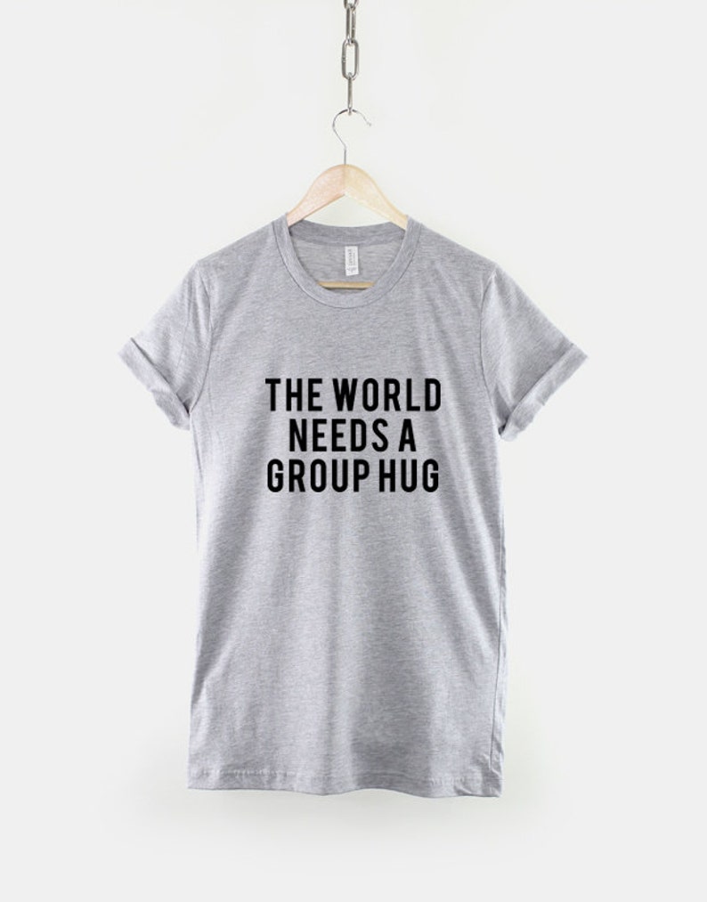 May include: A heather grey t-shirt with the text "THE WORLD NEEDS A GROUP HUG" printed in black.