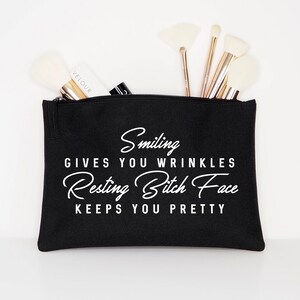 May include: Black cosmetic bag with the text "Smiling gives you wrinkles, Resting Bitch Face keeps you pretty" in white script. The bag is filled with makeup brushes and a tube of "Velour" brand makeup.