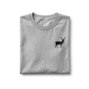 Puede incluir: Una camiseta de cuello redondo en color gris jaspeado que presenta una peque&ntilde;a silueta negra detallada de un ciervo de pie con astas bordada en el lado izquierdo del pecho. La prenda est&aacute; doblada cuidadosamente, mostrando el cuello.