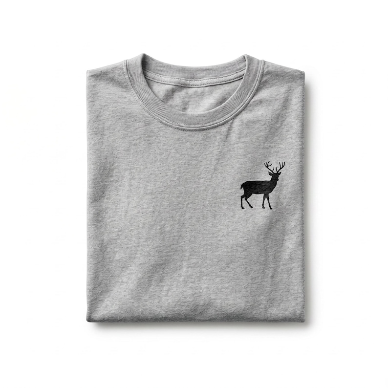 Puede incluir: Una camiseta de cuello redondo en color gris jaspeado que presenta una peque&ntilde;a silueta negra detallada de un ciervo de pie con astas bordada en el lado izquierdo del pecho. La prenda est&aacute; doblada cuidadosamente, mostrando el cuello.