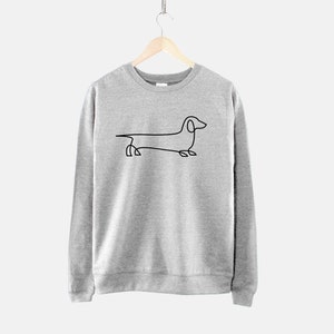 Może przedstawiać: Szara bluza z czarnym rysunkiem linii psa rasy dachshund na przodzie.