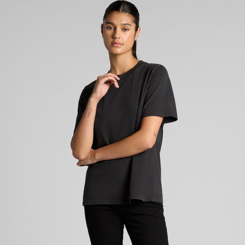 A woman wearing a black t-shirt stands with her arms crossed, looking directly at the camera.