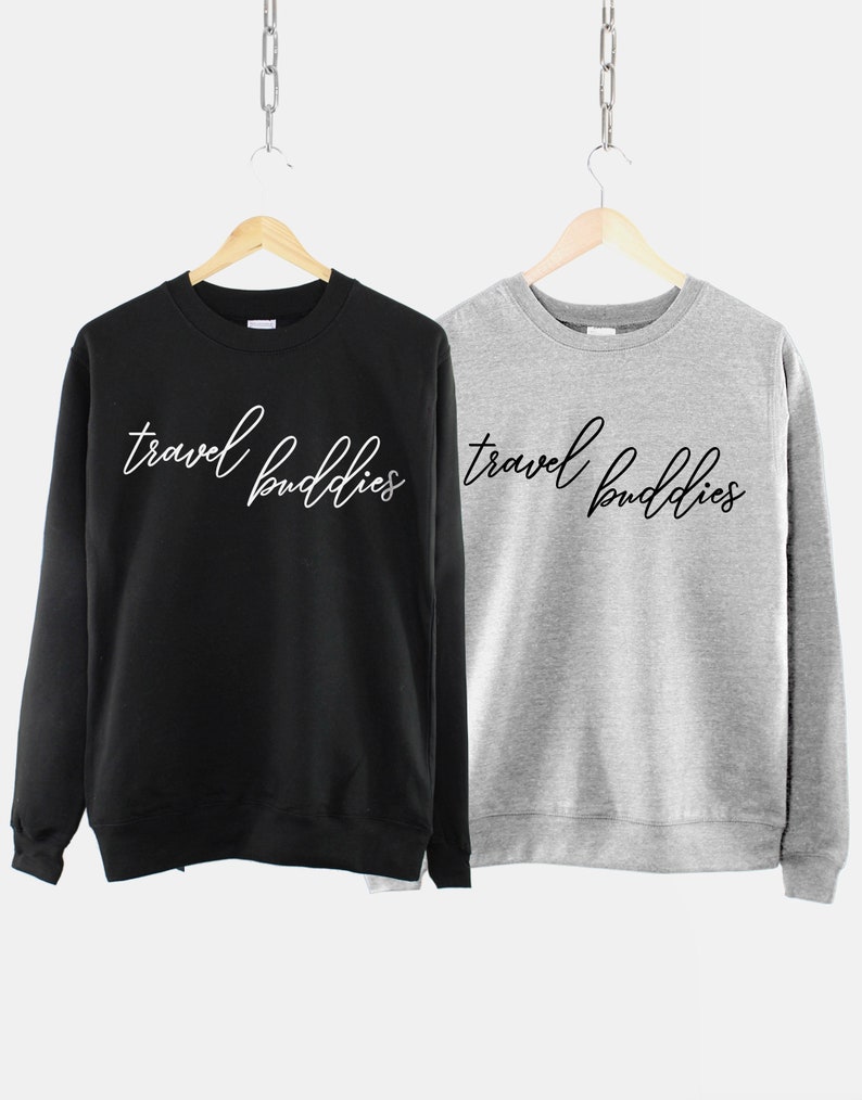 K&ouml;nnte beinhalten: Zwei Sweatshirts, eines schwarz und eines grau, mit dem Text "travel buddies" in wei&szlig;er Schrift auf der Vorderseite.