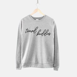 K&ouml;nnte beinhalten: Ein grauer Pullover mit dem Aufdruck "travel buddies" in Schwarz auf der Vorderseite.