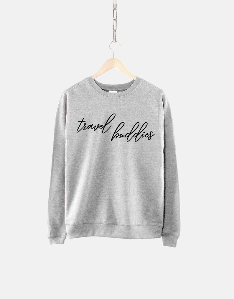 K&ouml;nnte beinhalten: Ein grauer Pullover mit dem Aufdruck "travel buddies" in Schwarz auf der Vorderseite.