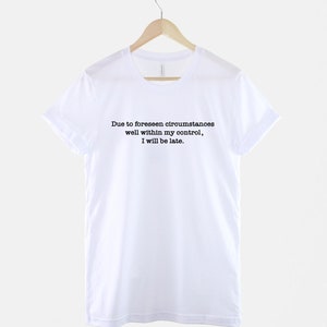 Op de afbeelding: Wit T-shirt met zwarte tekst die luidt: "Due to foreseen circumstances well within my control, I will be late."