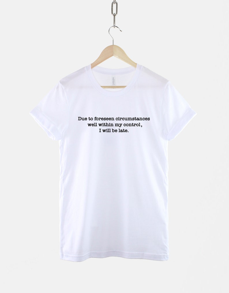 Op de afbeelding: Wit T-shirt met zwarte tekst die luidt: "Due to foreseen circumstances well within my control, I will be late."