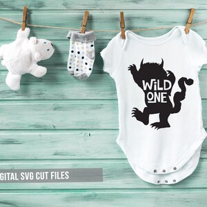 K&ouml;nnte beinhalten: Ein wei&szlig;er Baby-Body mit einer schwarzen Monstergrafik und dem Schriftzug "WILD ONE". Er h&auml;ngt an einer W&auml;scheleine zusammen mit einem wei&szlig;en Teddyb&auml;r und Socken mit Polka Dots. Der Hintergrund ist eine hellblaue Holzwand, mit dem Text "DIGITAL SVG CUT FILES".