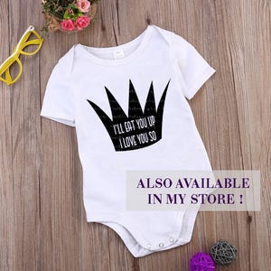 K&ouml;nnte beinhalten: Wei&szlig;er Baby-Body mit schwarzem Kronen-Motiv und dem Text "I'LL EAT YOU UP I LOVE YOU SO." Der Body hat kurze &Auml;rmel und Druckkn&ouml;pfe am unteren Ende. Der Text "ALSO AVAILABLE IN MY STORE !" ist ebenfalls sichtbar.