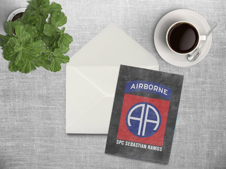 May include: A black card with a red, white, and blue military insignia. The insignia is a circle with the letters "AA" inside. The text "AIRBORNE" is above the insignia and the text "SPC SEBASTIAN RAMOS" is below the insignia.