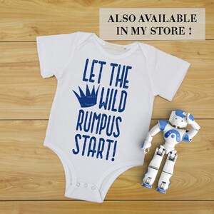 K&ouml;nnte beinhalten: Wei&szlig;er Baby-Body mit blauem Text "LET THE WILD RUMPUS START!" und blauer Krone. Ein kleines wei&szlig;es und blaues Roboterspielzeug liegt daneben. Der Text "ALSO AVAILABLE IN MY STORE!" steht oben.
