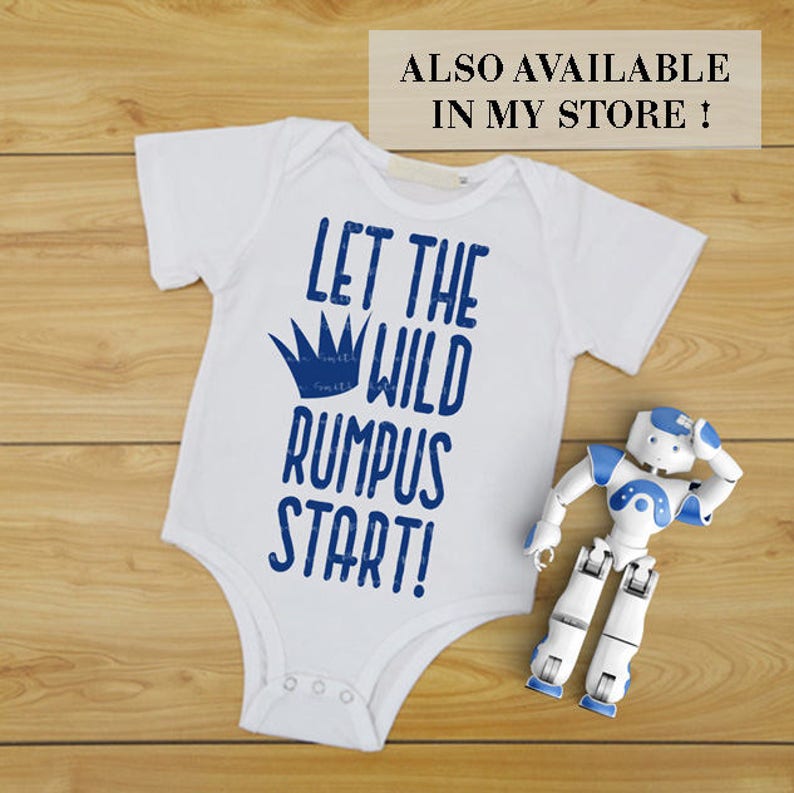 K&ouml;nnte beinhalten: Wei&szlig;er Baby-Body mit blauem Text "LET THE WILD RUMPUS START!" und blauer Krone. Ein kleines wei&szlig;es und blaues Roboterspielzeug liegt daneben. Der Text "ALSO AVAILABLE IN MY STORE!" steht oben.