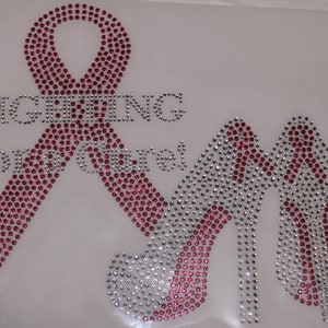 May include: Pink and silver rhinestone iron-on design featuring a ribbon and two high heels with the text "Fighting for our own".