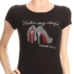 May include: Black short-sleeved t-shirt with a rhinestone design of a pair of red high heels. The shirt has the text "Under my steps" and "PSALM 119:133" printed on it.