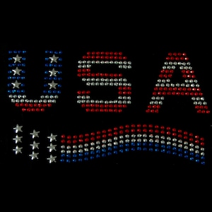 May include: USA spelled out in red, white, and blue rhinestones. A smaller version of the American flag is below the letters.