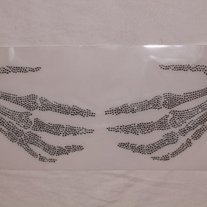 May include: Two silver skeleton hands made of rhinestones, on a white background.