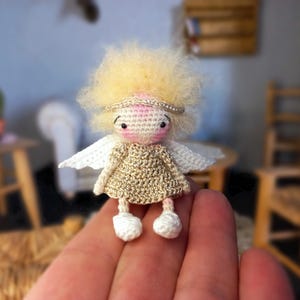 Peut inclure: Une poupée ange au crochet faite à la main, avec une robe dorée, des ailes blanches et des cheveux blonds duveteux. La poupée a un visage rose et un halo argenté. La poupée est petite et semble être tenue dans une main.