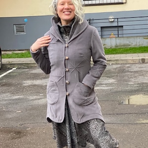May include: A woman wearing a gray jacket with a star pattern, a patterned skirt, and brown boots. She is standing in a puddle in front of a building.
