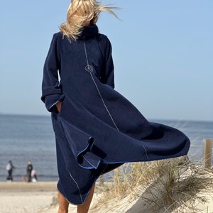 May include: A long, navy blue fleece dress with a high neck and long sleeves. The dress has a white line down the front and a small, embroidered spiral design on the chest.