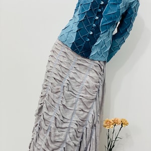 May include: A blue denim jacket with a textured design and a button closure. The jacket is paired with a light grey skirt with a gathered design.