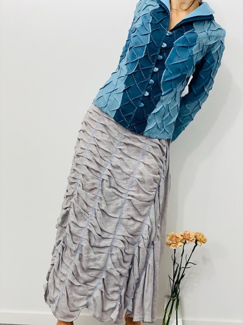 May include: A blue denim jacket with a textured design and a button closure. The jacket is paired with a light grey skirt with a gathered design.